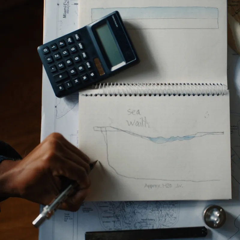 Hands sketching a seawall cross-section on graph paper with calculator and Cape Coral canal map